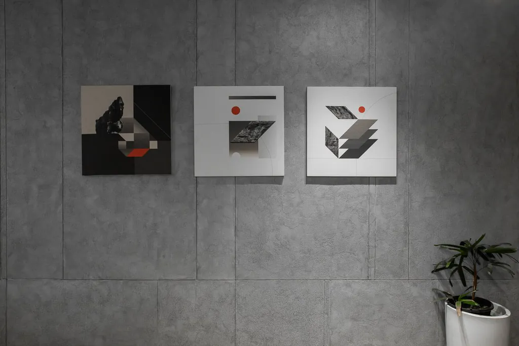 Three abstract geometric artworks on a textured grey concrete-panel wall, with a potted plant in the corner