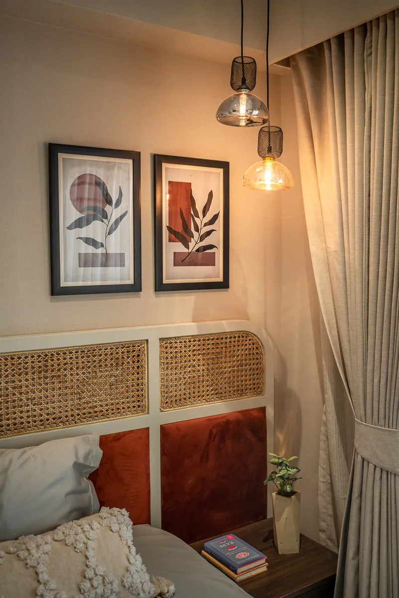 Bedroom corner with two framed leaf prints above a cane and rust-velvet headboard, lit by glass pendant lamps
