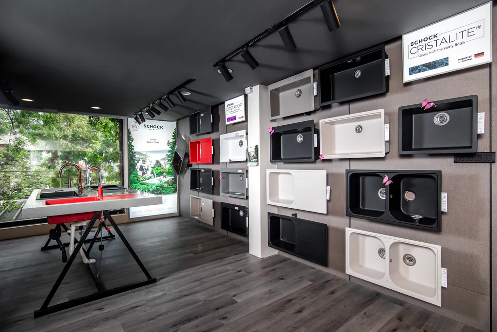 Showroom wall displaying kitchen sinks in black, white, grey and red, with a demo counter by the window