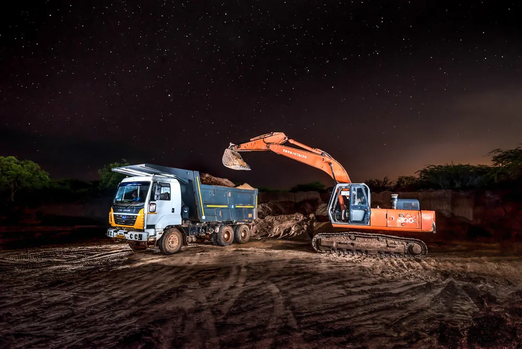 A Tata Hitachi excavator loading an Ashok Leyland dump truck at night under a sky full of stars