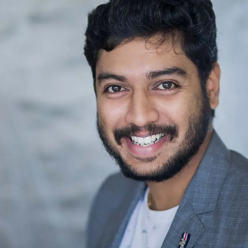 Portrait of Pradeep Sekar, smiling, in a grey blazer