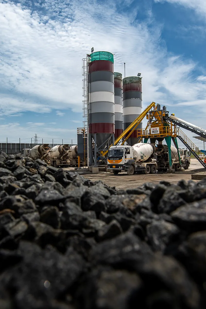 Concrete batching plant silos and transit mixer trucks behind a heap of aggregate