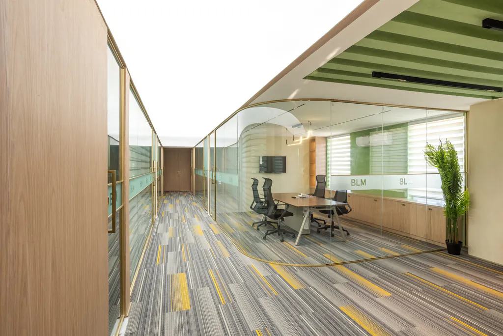 Office corridor with glass-walled cabins, a striped carpet and a plant at the far end