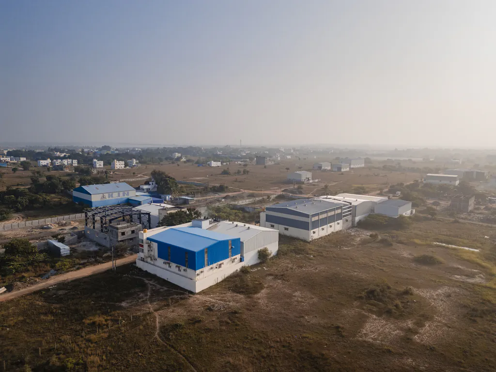 Drone view of factory sheds with blue roofs surrounded by open land